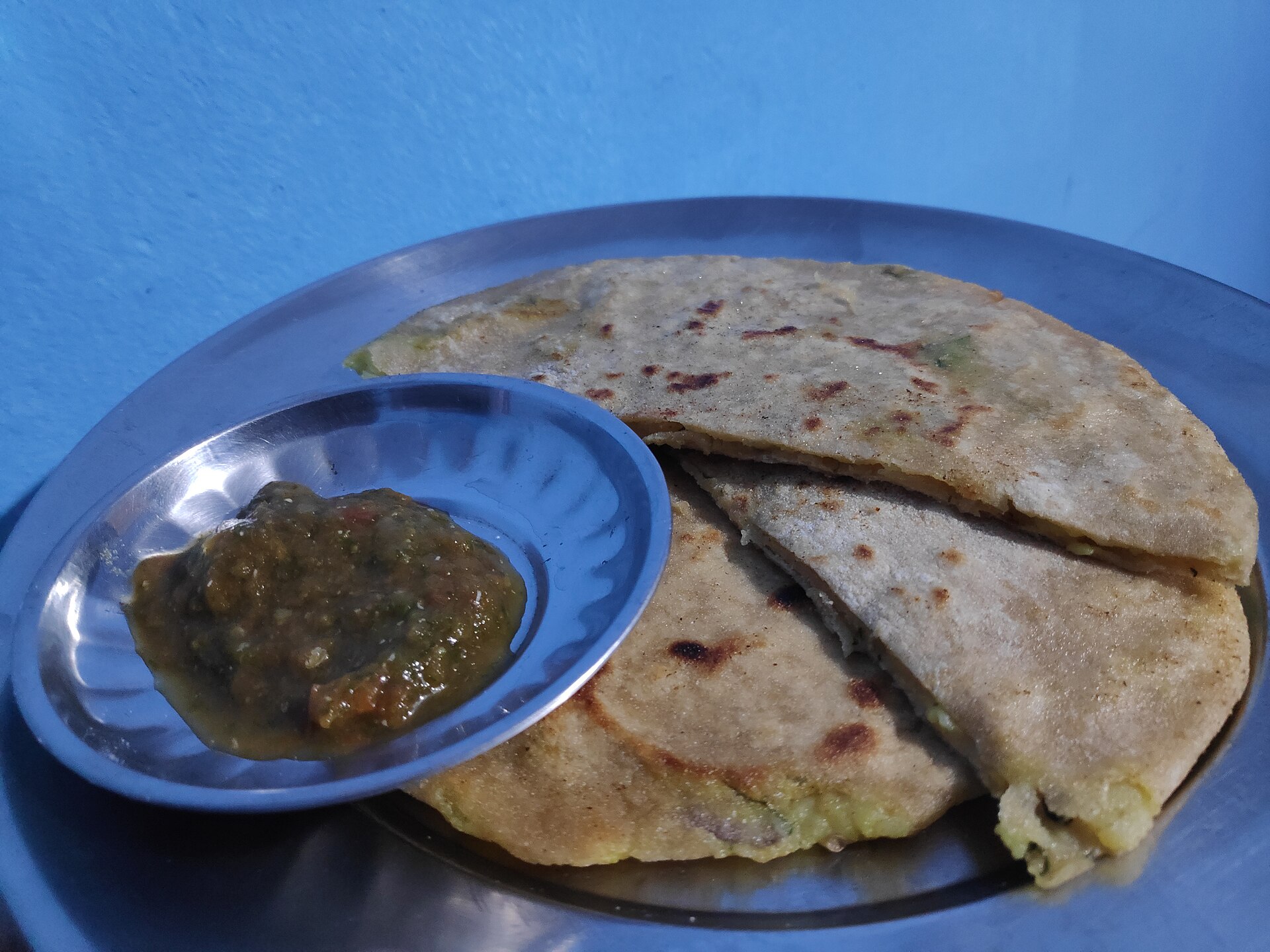 Stuffed parathas with a bowl of chutney on a blue plate