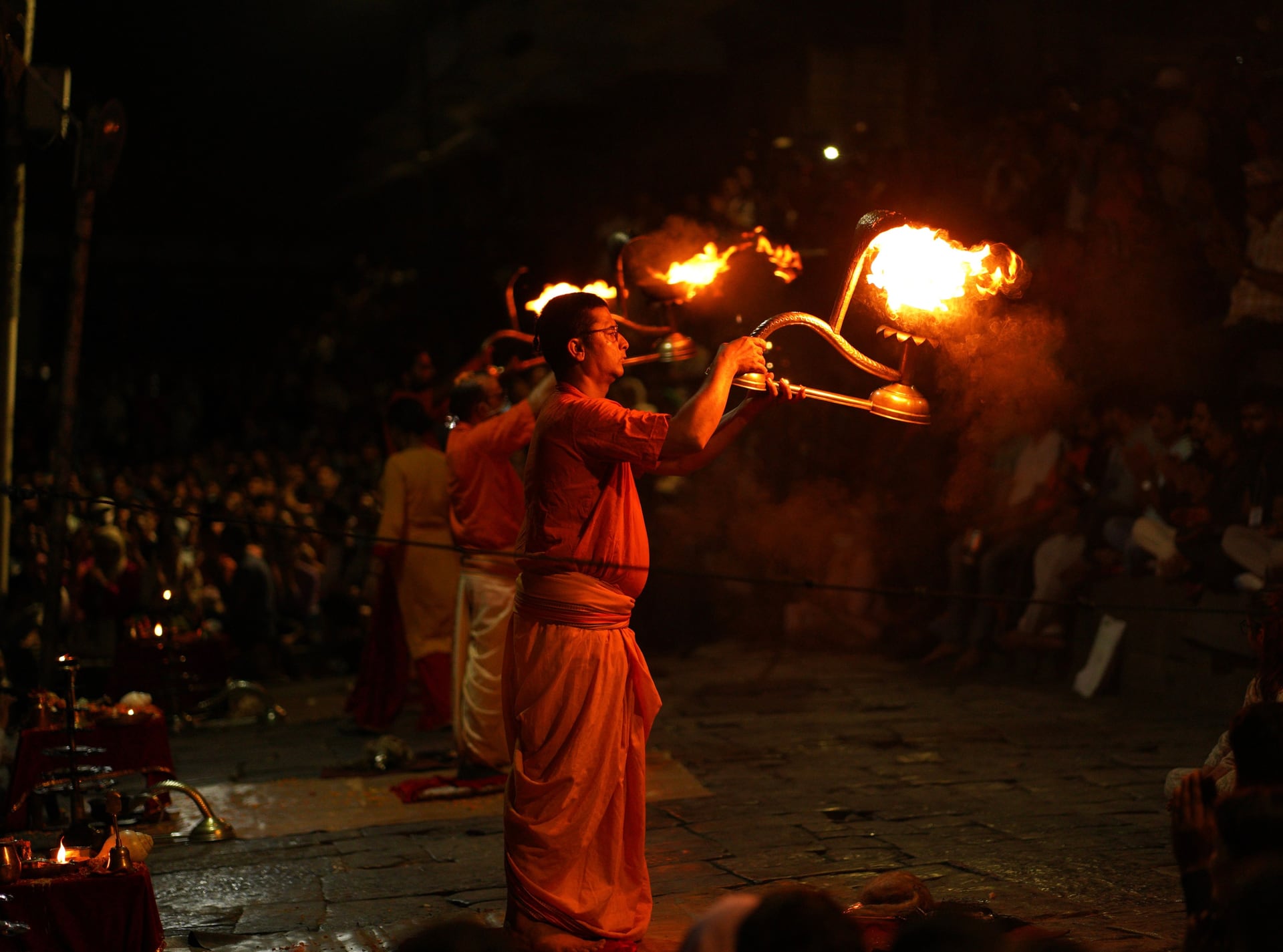 Varanasi — priests in saffron raise flaming brass lamps at the evening Ganga aarti, crowds watching from the ghat