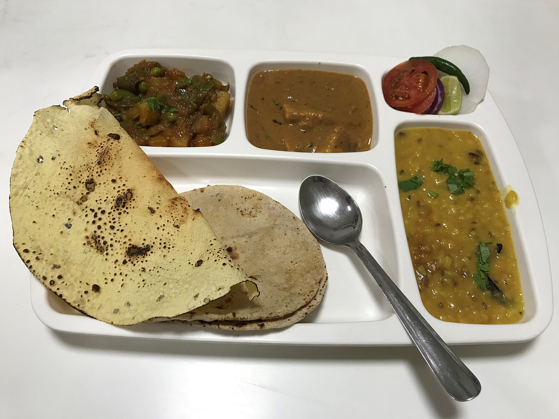 A North Indian vegetarian meal in a compartment plate: dal, sabzi, salad and roti