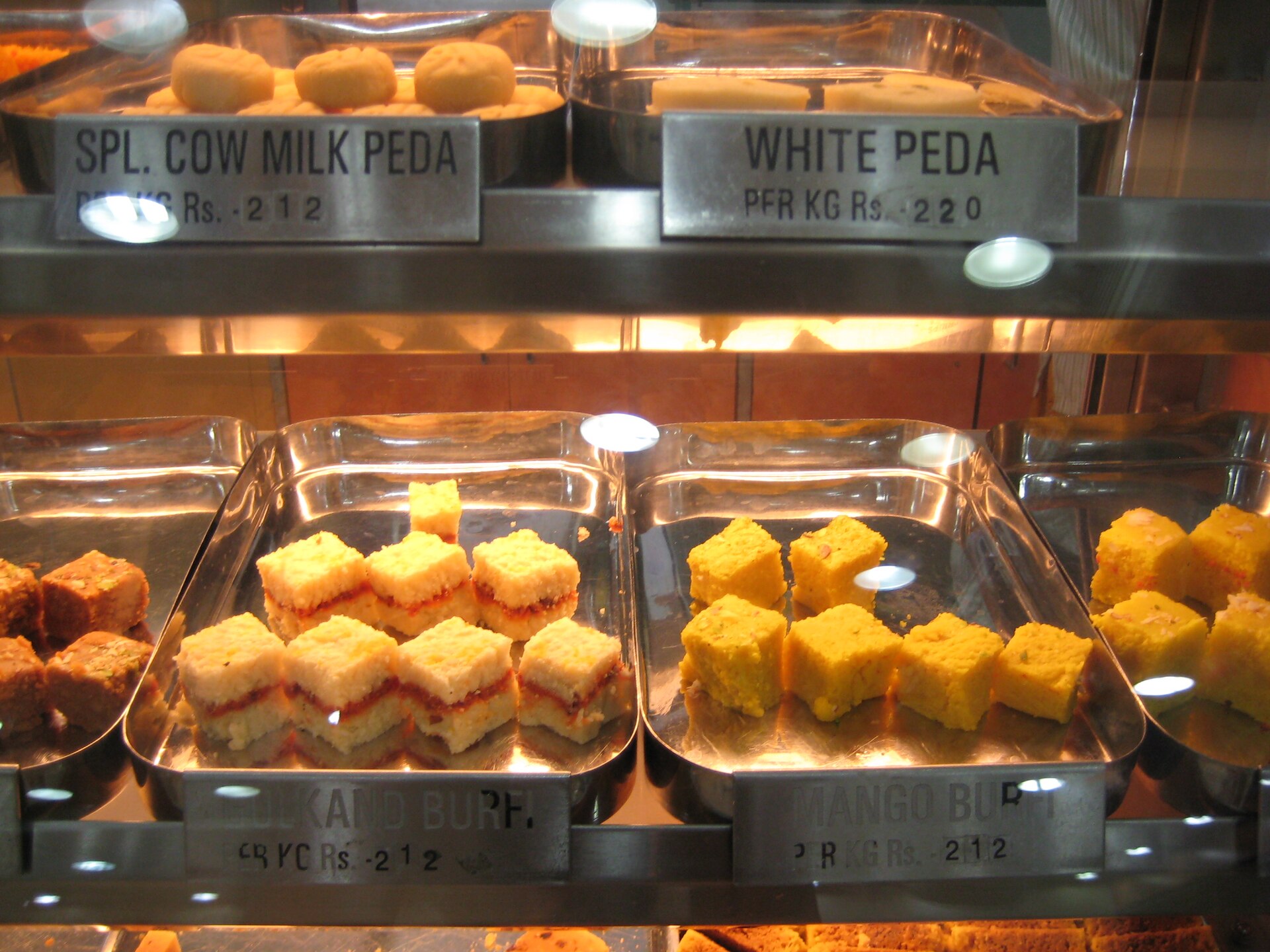 Peda and milk sweets on trays behind a sweet-shop counter