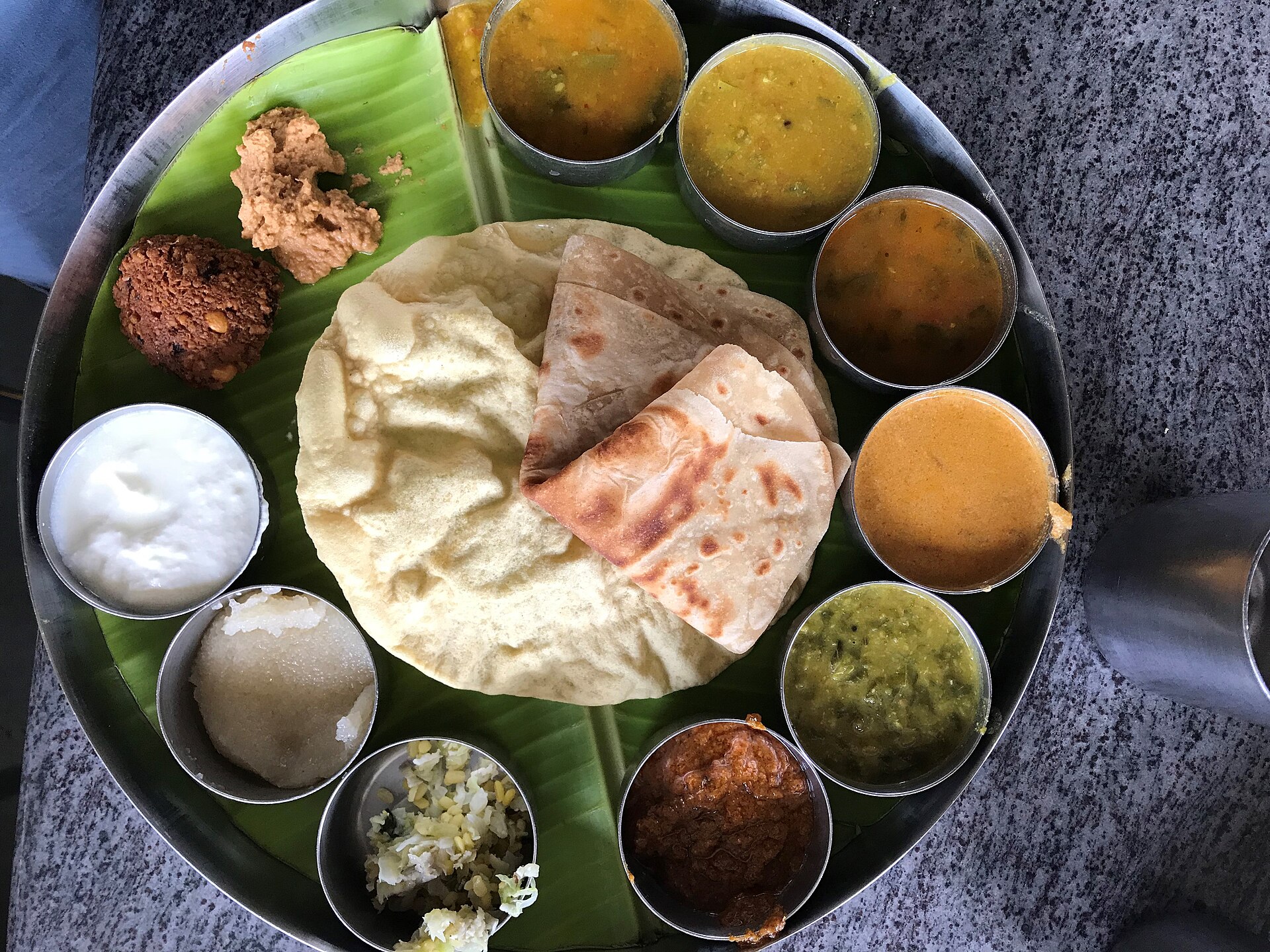 A vegetarian thali on a banana leaf with a dozen small bowls of dal, sabzi, raita and sweets